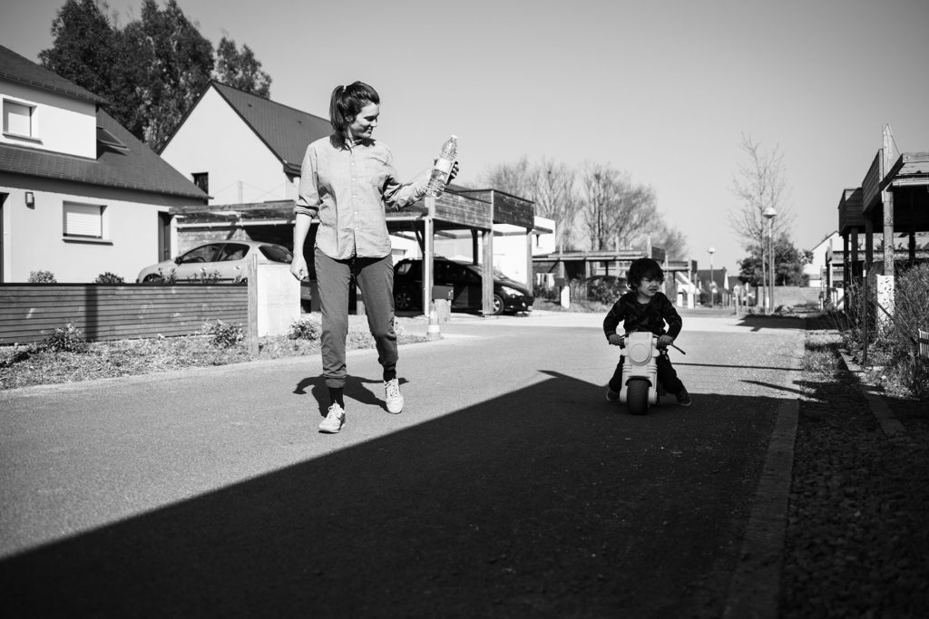 Reportage du quotidien près de Rennes. Photographie en noir et blanc d'une maman et de son fils en vélo à l'extérieur.