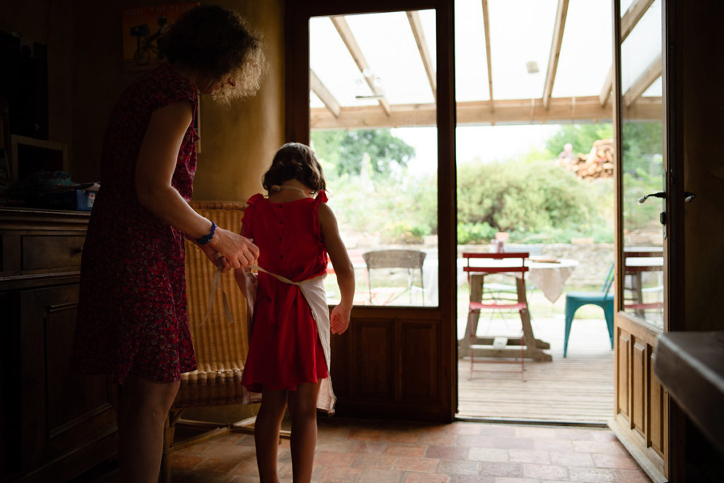 Mon projet photo 52 : qu’est-il devenu ? Reportage du quotidien, une maman attache un tablier à sa fille qui s'apprête à faire de la cuisine.