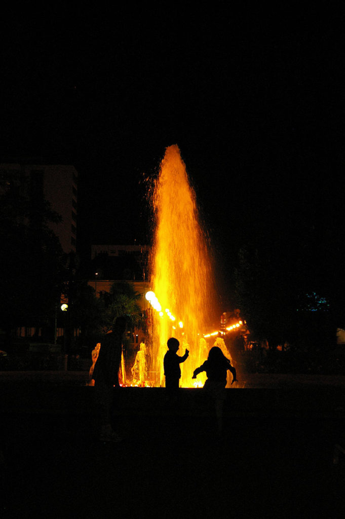 "10 years challenge" : mon évolution photographique. Photo de nuit en contre-jour avec des enfants qui jouent devant une fontaine illuminée.