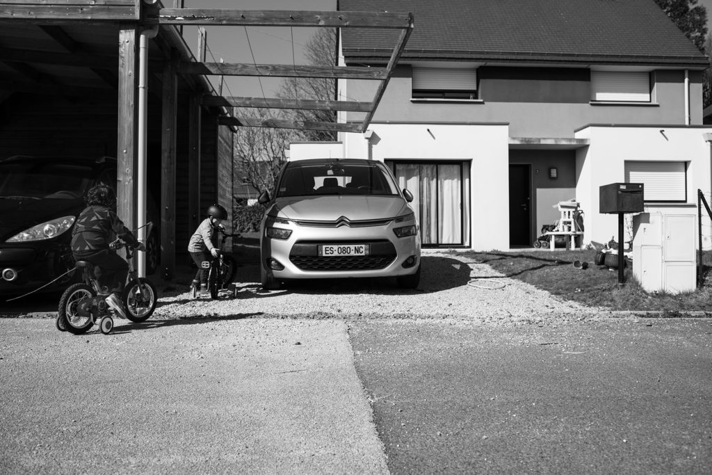 Reportage du quotidien près de Rennes. Photographie en noir et blanc d'enfants jouant devant une maison.