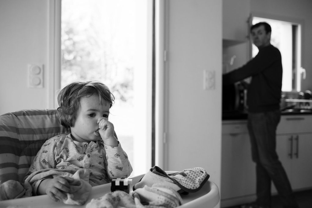 Reportage du quotidien près de Rennes. Photographie en noir et blanc d'un enfant à peine réveillé et de son papa préparant son gouter.
