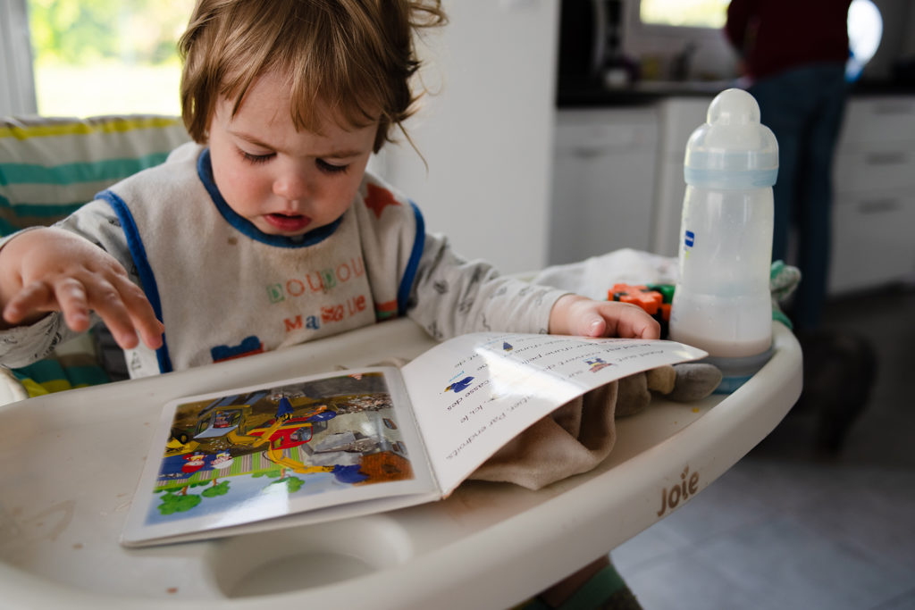 Reportage du quotidien près de Rennes. Photographie d'un jeune enfant dans sa chaise haute lisant un livre.