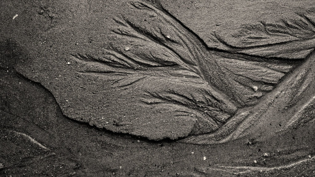Photographe, apprendre à lâcher prise. Photographie en noir et blanc de dessins laissés par l'eau sur le sable.