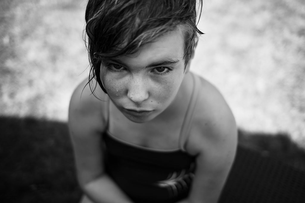 Pourquoi je fais le choix de la photographie en noir et blanc ? Portrait en noir et blanc d'une jeune fille. Ses taches de rousseur ressortent par contraste ainsi que des gouttes d'eau sur son visage.