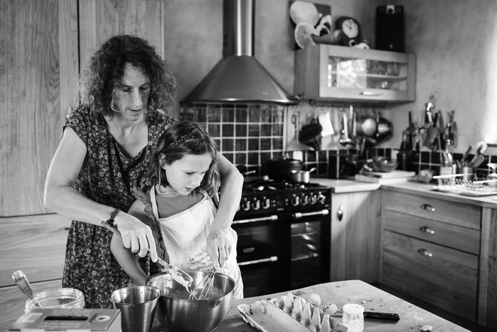 Pourquoi je fais le choix de la photographie en noir et blanc ? Photographie en noir et blanc d'une scène de vie de famille. Reportage du quotidien, une maman prépare un gâteau avec sa fille.
