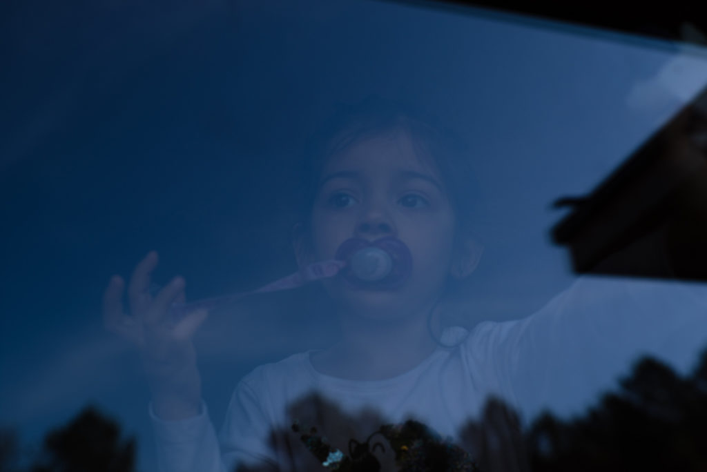 Comment mon hypersensibilité me sert en tant que photographe ? Portrait à travers une fenêtre d'une petite fille. La couleur bleue nuit dominante et l'effet de reflet donnent un caractère irréel à l'image. Photographe Pascaline Michon