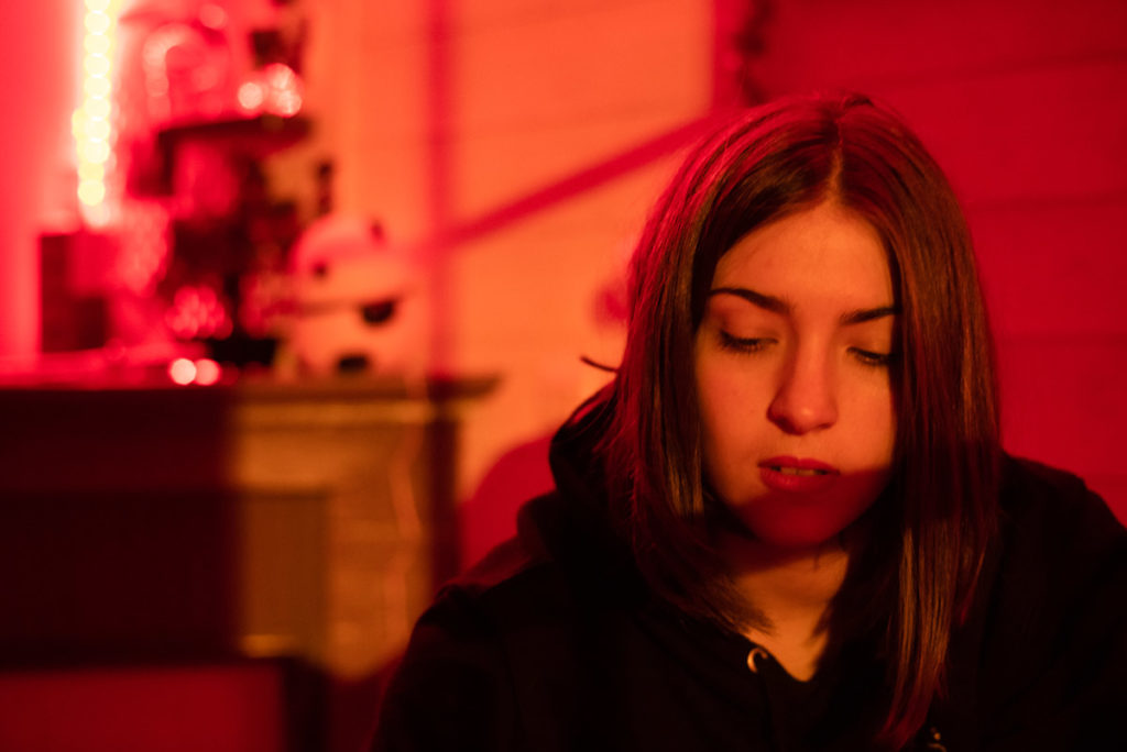 Portraits en lumière colorée. Portrait d'une ado dans sa chambre,en basse lumière,ambiance colorée en rouge. Photographe Pascaline Michon.
